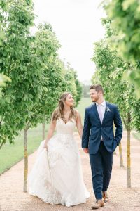 bride and groom holding hands and walking through rows of trees