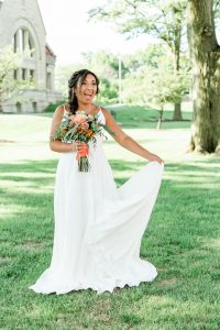 bride holding bouquet and train off dress on lawn