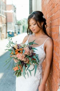 bride looking at bouquet and leaning against brick wall