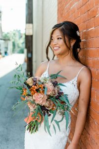 bride holding bouquet and leaning against brick wall
